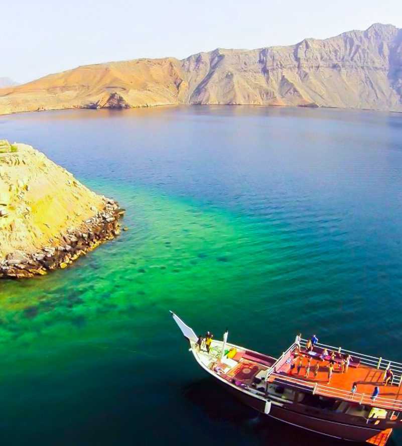 A boat glides on the water, surrounded by a majestic mountain-Dhow Cruise Tour In Khasab Musandam