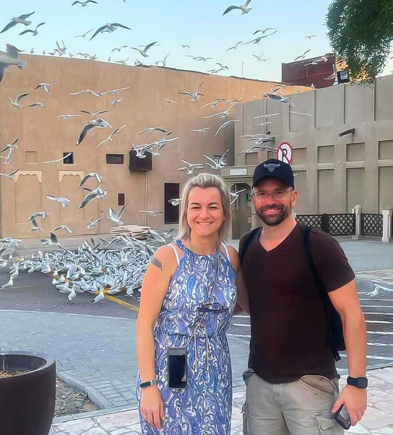 A couple smiling for a picture with a group of birds in the background Dubai