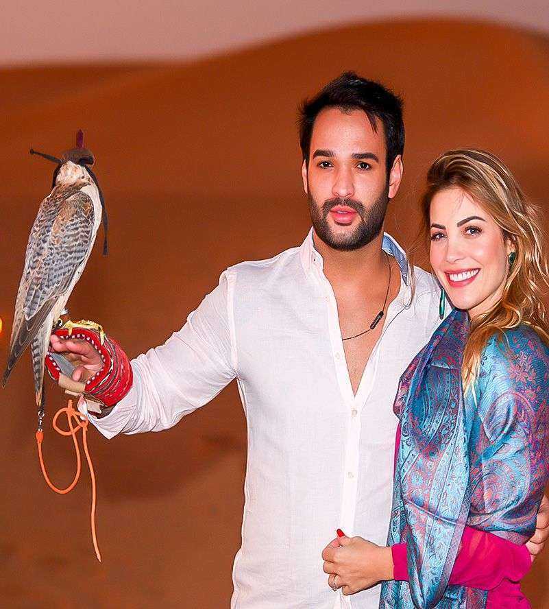 A man and woman standing in the Dubai desert, surrounded by vast sandy dunes