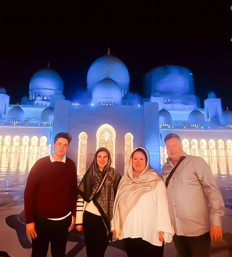 A nighttime scene featuring three people standing in front of Sheikh Zayed Grand MosqueA woman gracefully strolling in front of a grand white building Sheikh Zayed Grand Mosque