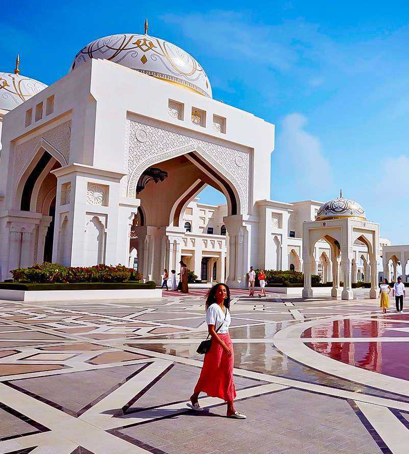 A woman gracefully strolling in front of a grand white building Sheikh Zayed Grand Mosque-Qasr Al Watan