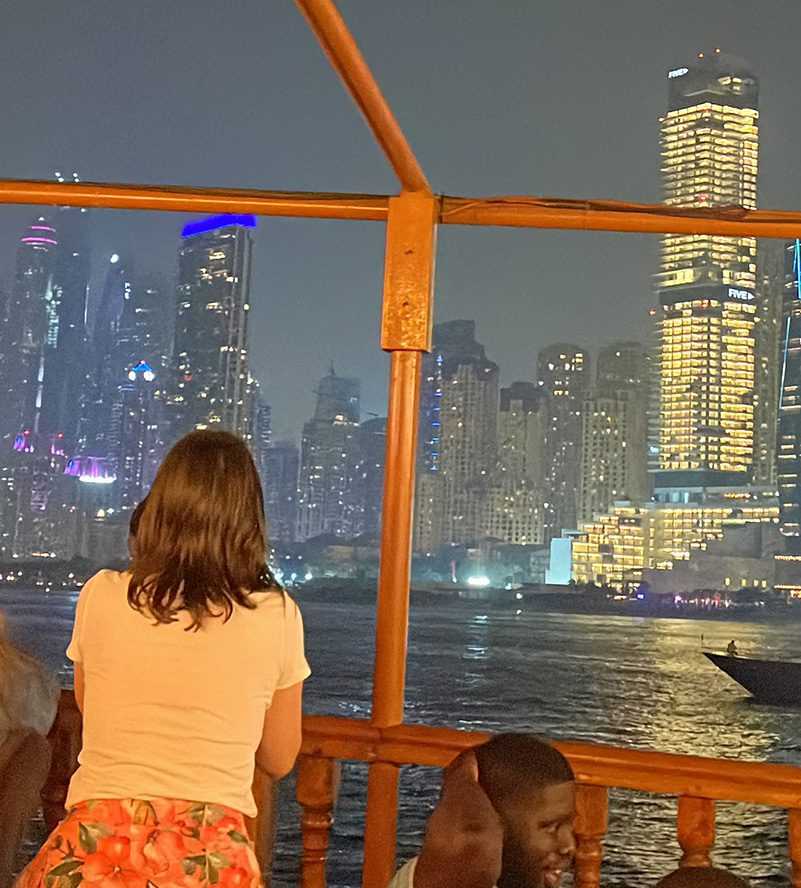 A woman on a boat gazes at the city at night, captivated by the mesmerizing urban lights-Cruise Dubai