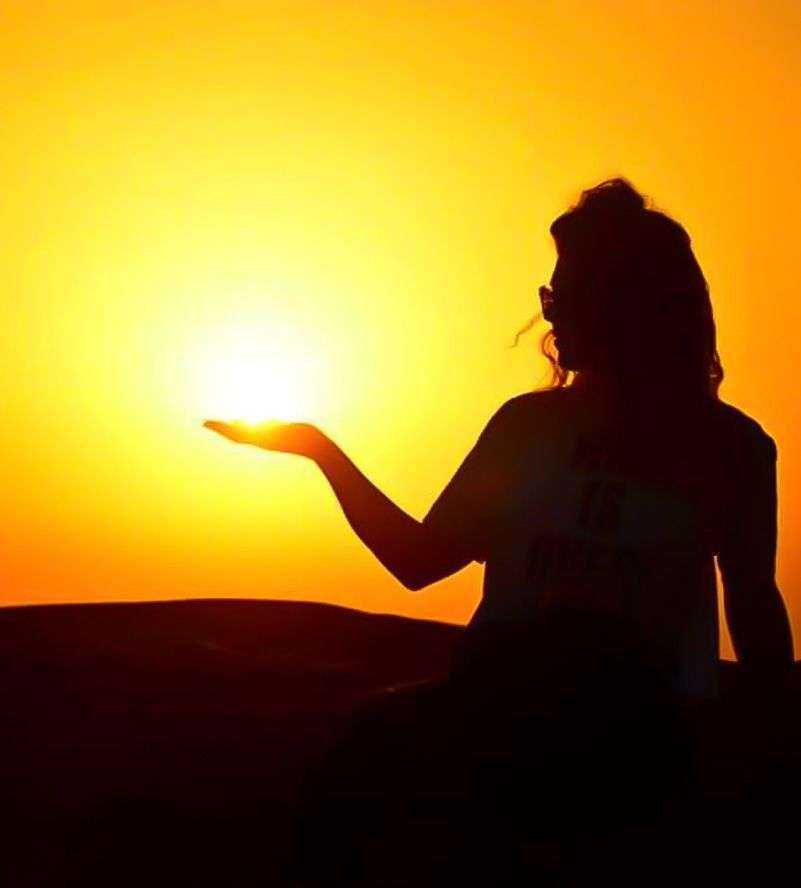 A woman silhouetted against the sun, extending her hand Dubai desert