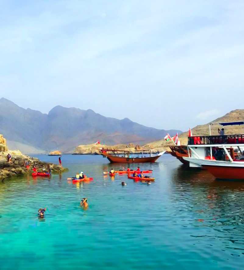 Boats sailing near mountains and a beach, creating a picturesque scene of tranquility and natural beauty-Dhow Cruise Tour In Khasab Musandam