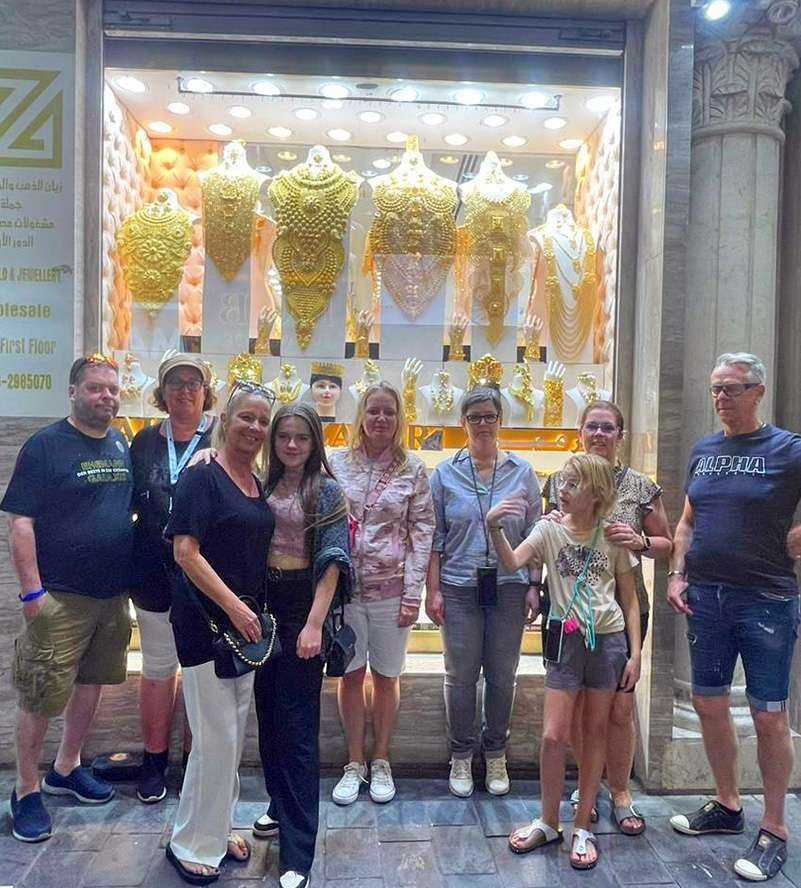 Dubai Gold Souk A group of individuals standing proudly in front of a gleaming gold shop, showcasing their joy and admiration for the precious metal