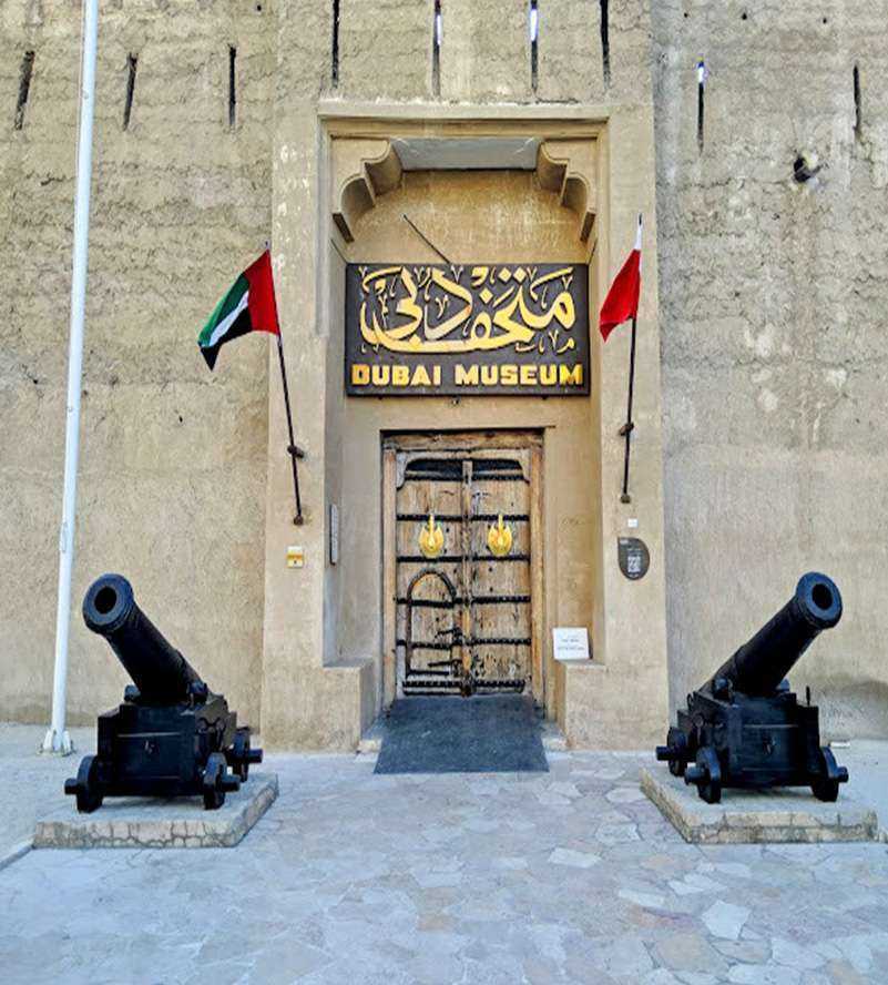 Dubai Museum Two cannons positioned in front of a flag-adorned buildin
