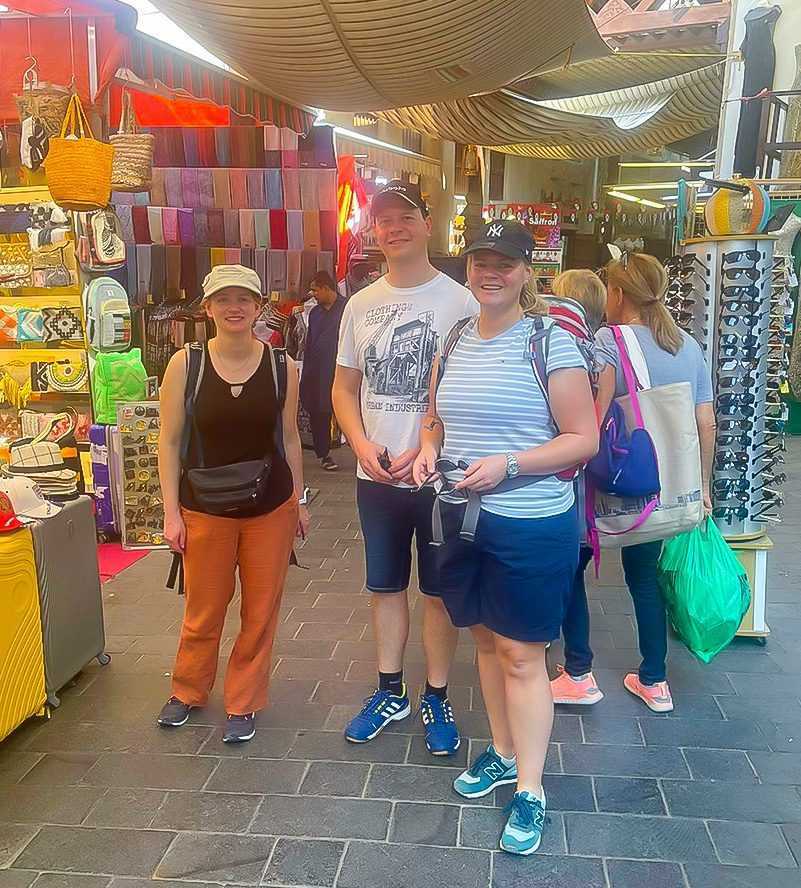 Three individuals standing in front of a bustling market dubai
