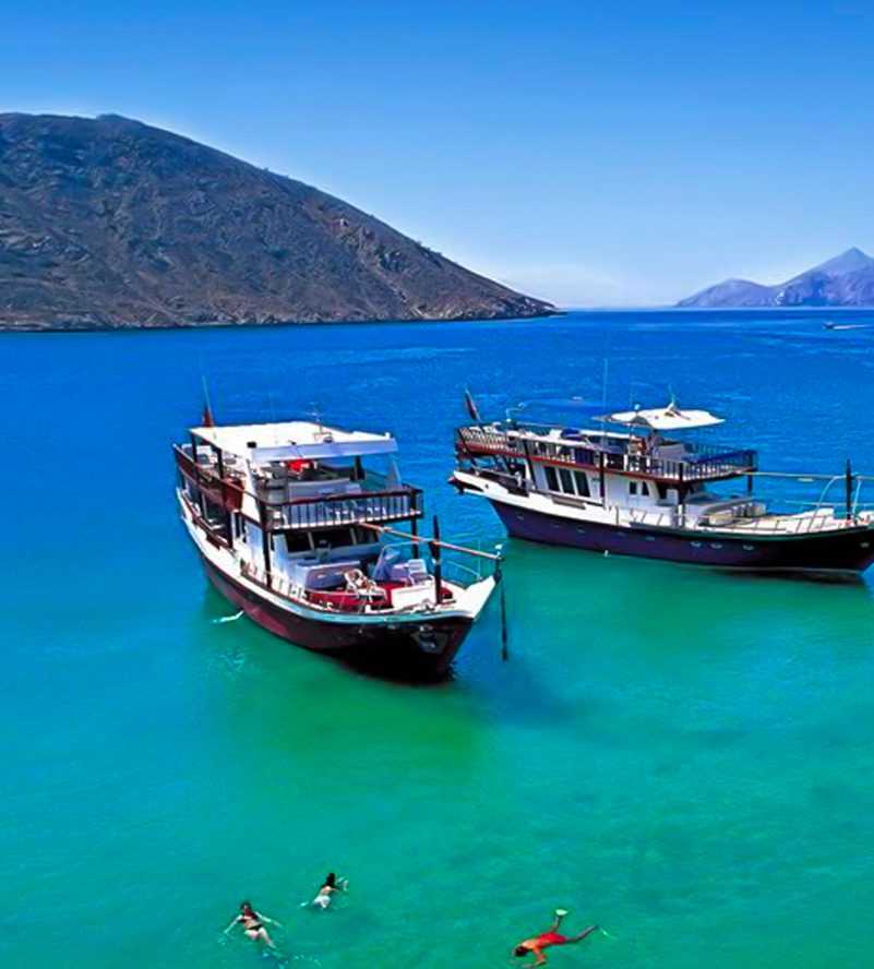 Two boats peacefully anchored in crystal-clear blue water, creating a serene and picturesque scene-Dhow Cruise Tour In Khasab Musandam