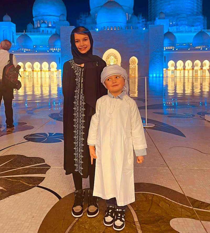 Two children in traditional clothing smiling for a photo in front of the Sheikh Zayed Grand MosqueA woman gracefully strolling in front of a grand white building Sheikh Zayed Grand Mosque