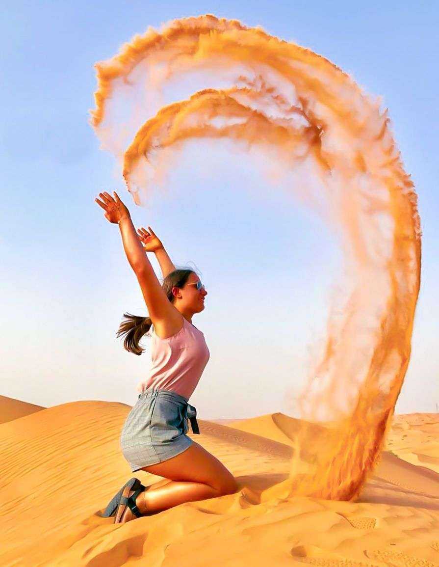 a girl kneeling in the desert with orange sand Dubai