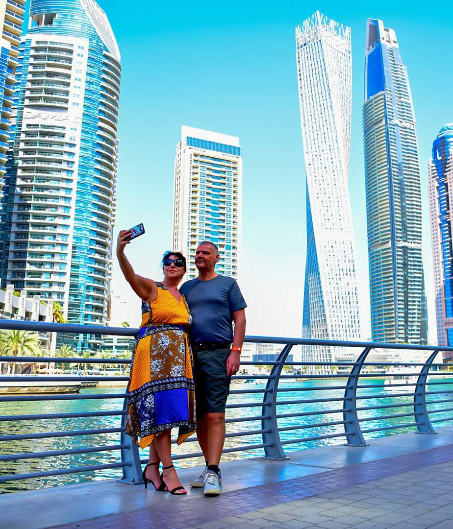 couple smiling while taking a selfie in front of a bustling cityscape