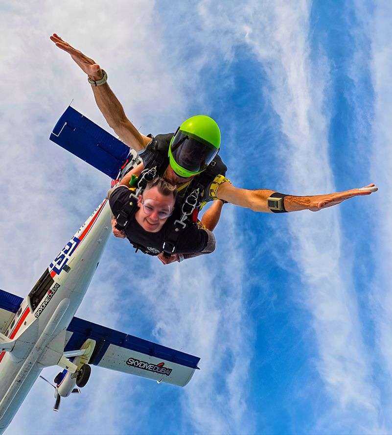 person in skydiving suit and helmet with another person in the air