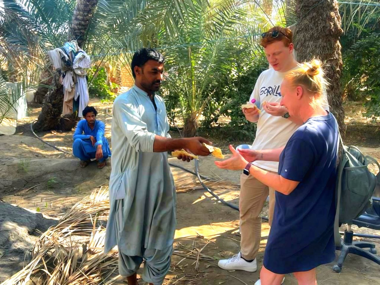 ChatGPT said: Deutsche nehmen frisch gebackenes Brot von einem Oasenarbeiter – traditionelles Erlebnis und kulturelles Highlight in Al Ain, VAE.