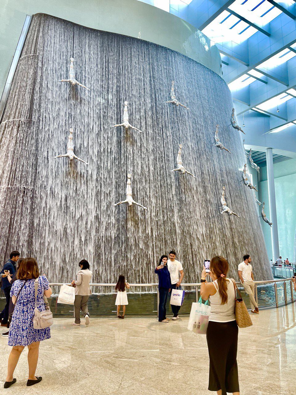Wasserfall in der Dubai Mall mit der beeindruckenden Perlentaucher-Skulptur – eine Hommage an Dubais Vergangenheit als Fischerdorf und Zentrum des Perlenhandels, beliebtes Fotomotiv und Highlight für Besucher.