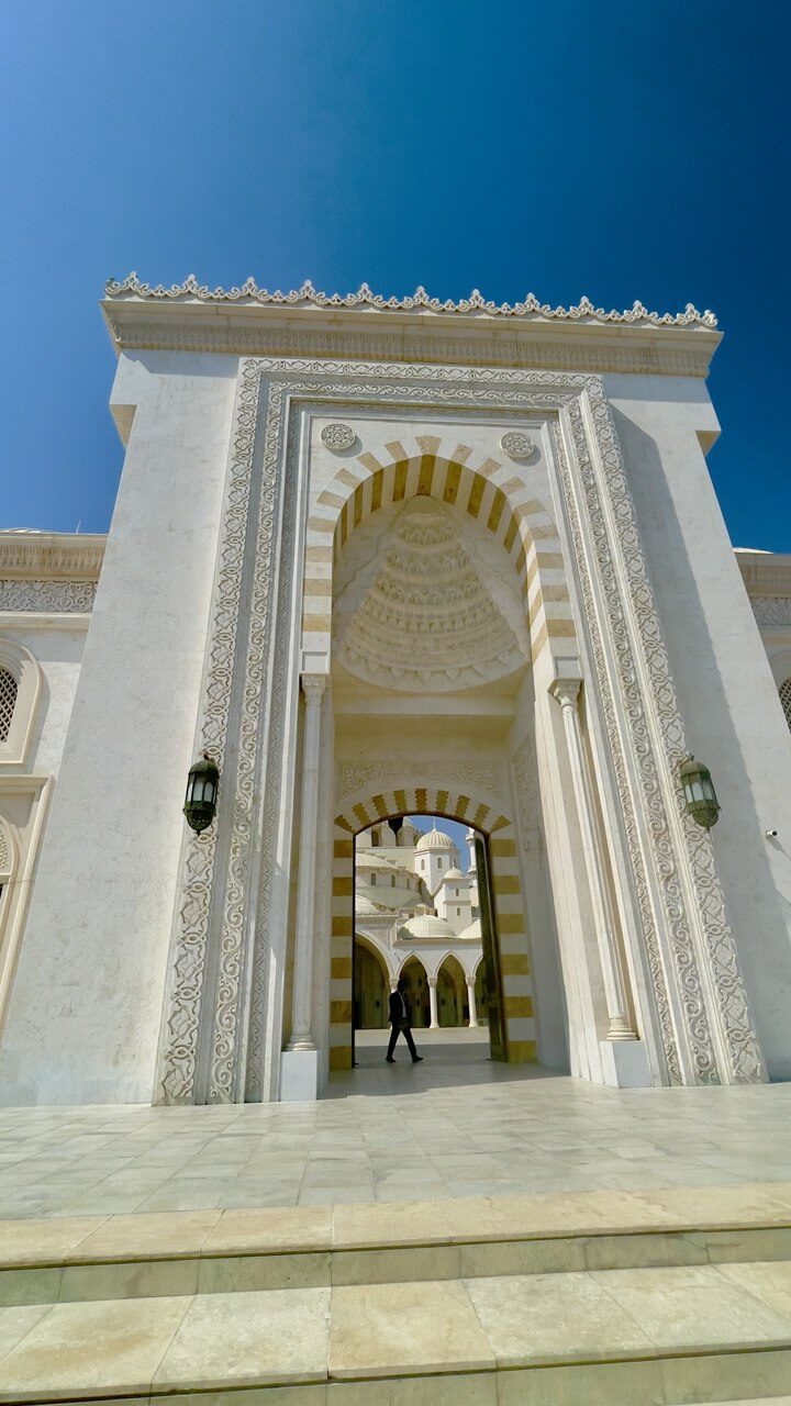 Haupteingang der Moschee – verziert mit weißem Granit, öffnet sich zum Innenhof, den Arkaden und Kuppeln, beeindruckendes architektonisches Highlight und beliebtes Touristenziel in den VAE.