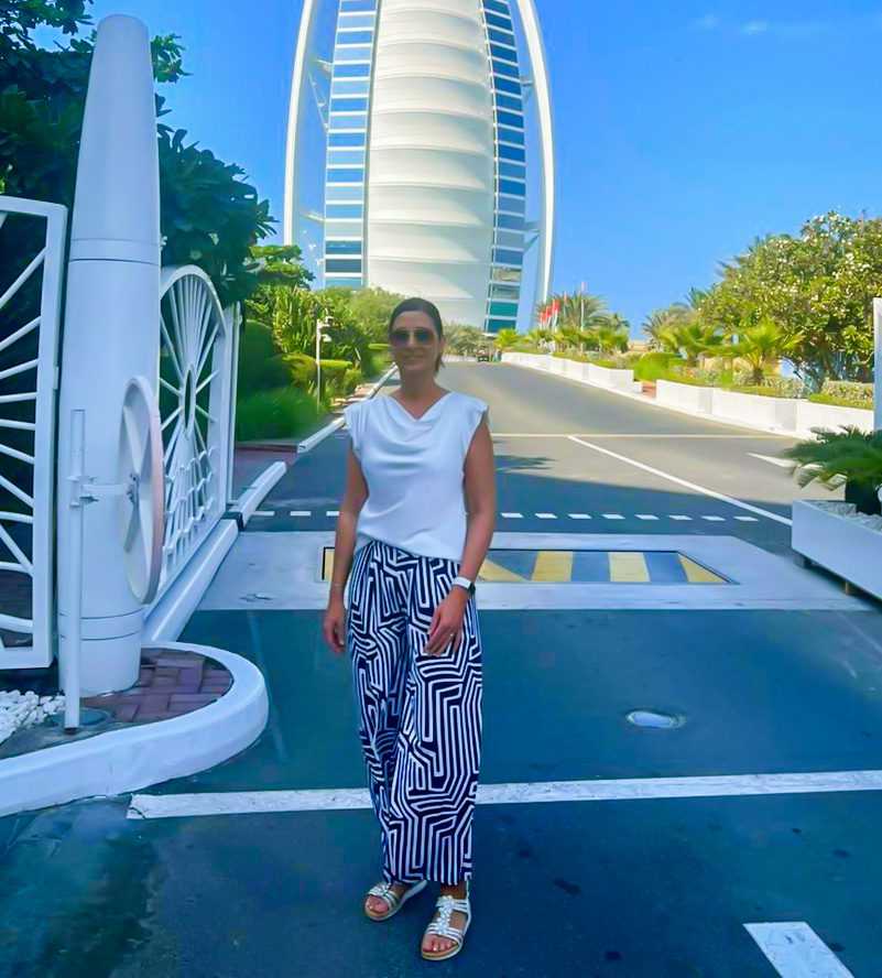 woman in a white shirt and blue:white striped pants posing in front of the iconic Burj Al Arab-Dubai Sightseeing Tour